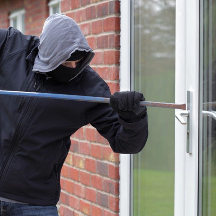 Un cambrioleur tentant de forcer une porte-fenêtre avec un pied-de-biche, mettant en évidence l'importance des dispositifs de sécurité anti-effraction pour protéger les habitations.